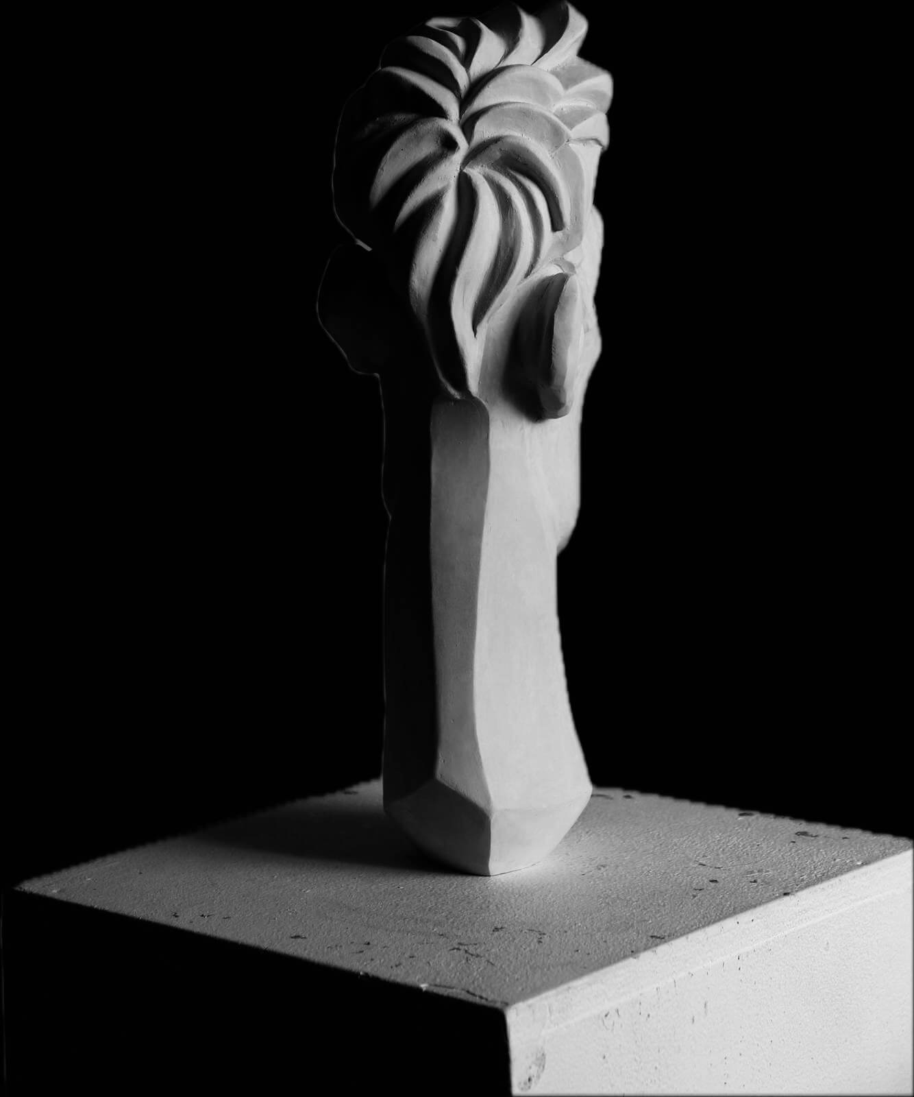 Achterzijde van het langgerekte gestileerde portret. Het haar en de nek zijn vloeiend gemodelleerd, met een spel van lijnen en vormen die in elkaar overvloeien.