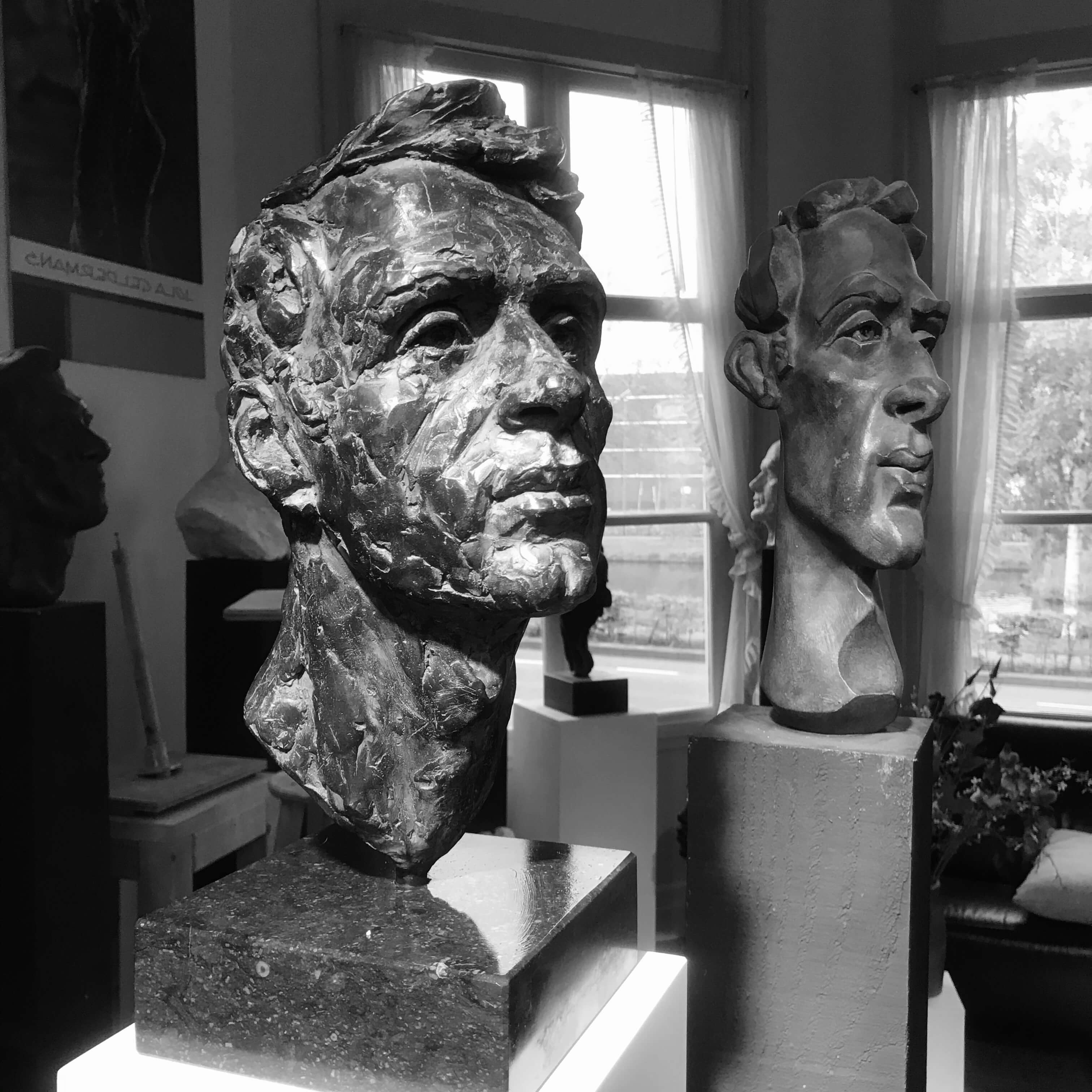 Twee beelden naast elkaar: links een realistisch bronzen portret van een man, rechts een langgerekte, gestileerde interpretatie van hetzelfde model. Beide tonen verschillende facetten van zijn persoonlijkheid.